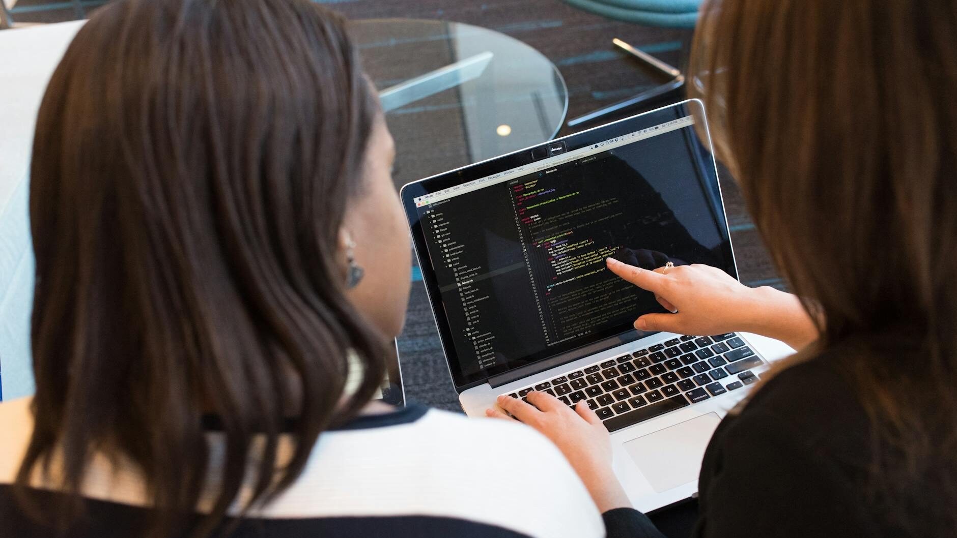 Two women working together on software programming indoors, focusing on code.